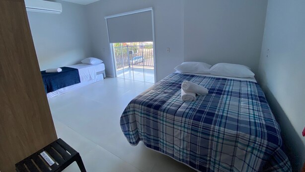 A bedroom with a bed, a small desk, and a sliding door leading to a balcony. - Pousada Ametista (Penha)