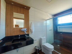Un baño moderno con un lavamanos negro, un inodoro blanco, un box de ducha de vidrio y un mueble de tocador de madera con espejo.