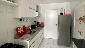 A compact kitchen with white cabinets, a stainless steel refrigerator, a gas stove, and a microwave. - 1101 Ap Vista mar atrás da passarela (Aracaju)