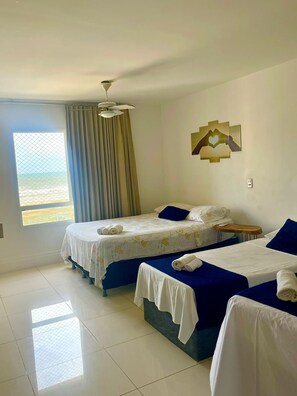 A hotel room with two beds, a ceiling fan, a window with curtains, and a wall decoration. - 1101 Ap Vista mar atrás da passarela (Aracaju)
