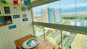 A balcony with a tiled floor, a wooden table with a plate, and a view of buildings and a construction site. - 1101 Ap Vista mar atrás da passarela (Aracaju)