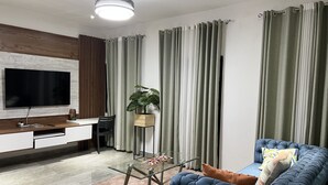 A modern living room with a flat-screen TV, a blue sofa, a glass coffee table, and a wooden sideboard. - A Haven of Comfort in Labone, with easy access to essentials amenities (Accra)