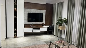 A modern living room with a flat-screen TV mounted on a wooden wall, a glass coffee table, and a sofa. - A Haven of Comfort in Labone, with easy access to essentials amenities (Accra)