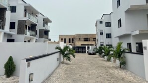 A modern residential area with white buildings, a paved pathway, and palm trees. - A Haven of Comfort in Labone, with easy access to essentials amenities (Accra)