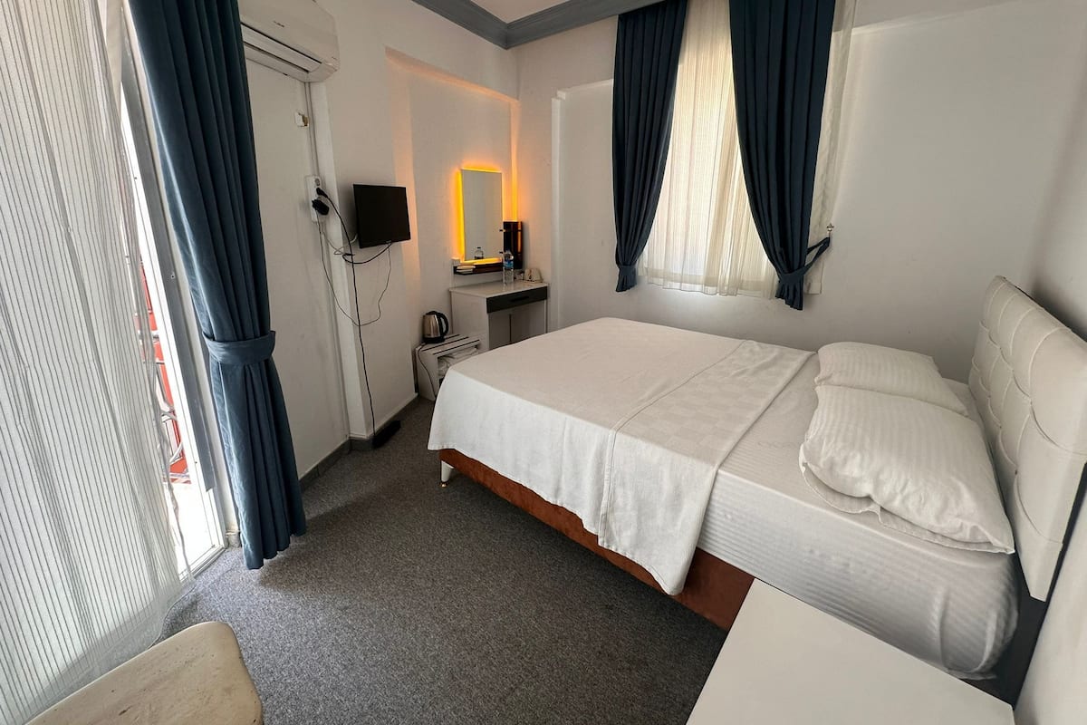 Ein Hotelzimmer mit Bett, Schreibtisch, Stuhl, Fernseher und einem Vorhangfenster.