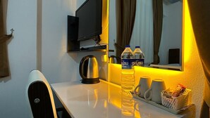 Une chambre d’hôtel équipée d’un téléviseur à écran plat fixé au mur, d’une table avec une bouilloire, de deux bouteilles d’eau, d’une tasse et d’un panier de collations.