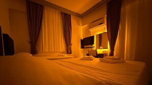 Une chambre d’hôtel avec deux lits, un téléviseur à écran plat, un bureau avec une chaise et une fenêtre avec des rideaux.