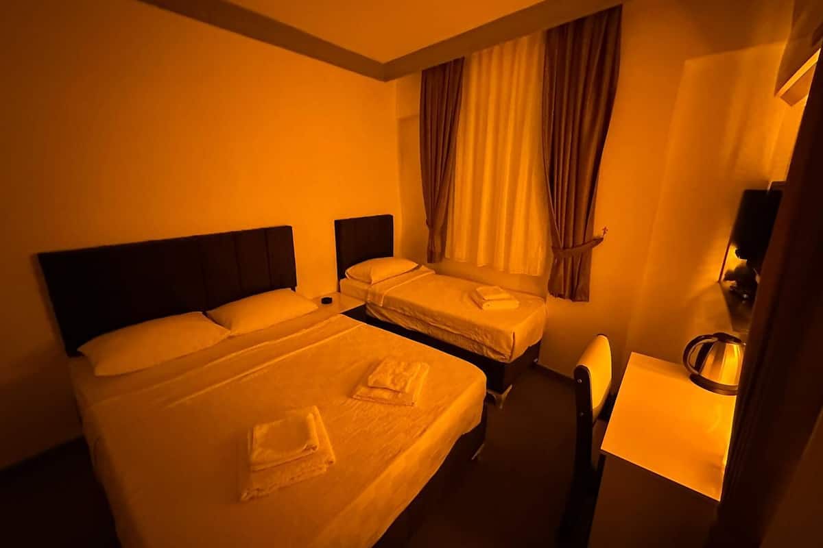 Ein Hotelzimmer mit zwei Betten, einem kleinen Schreibtisch und einem Fenster mit Vorhängen.