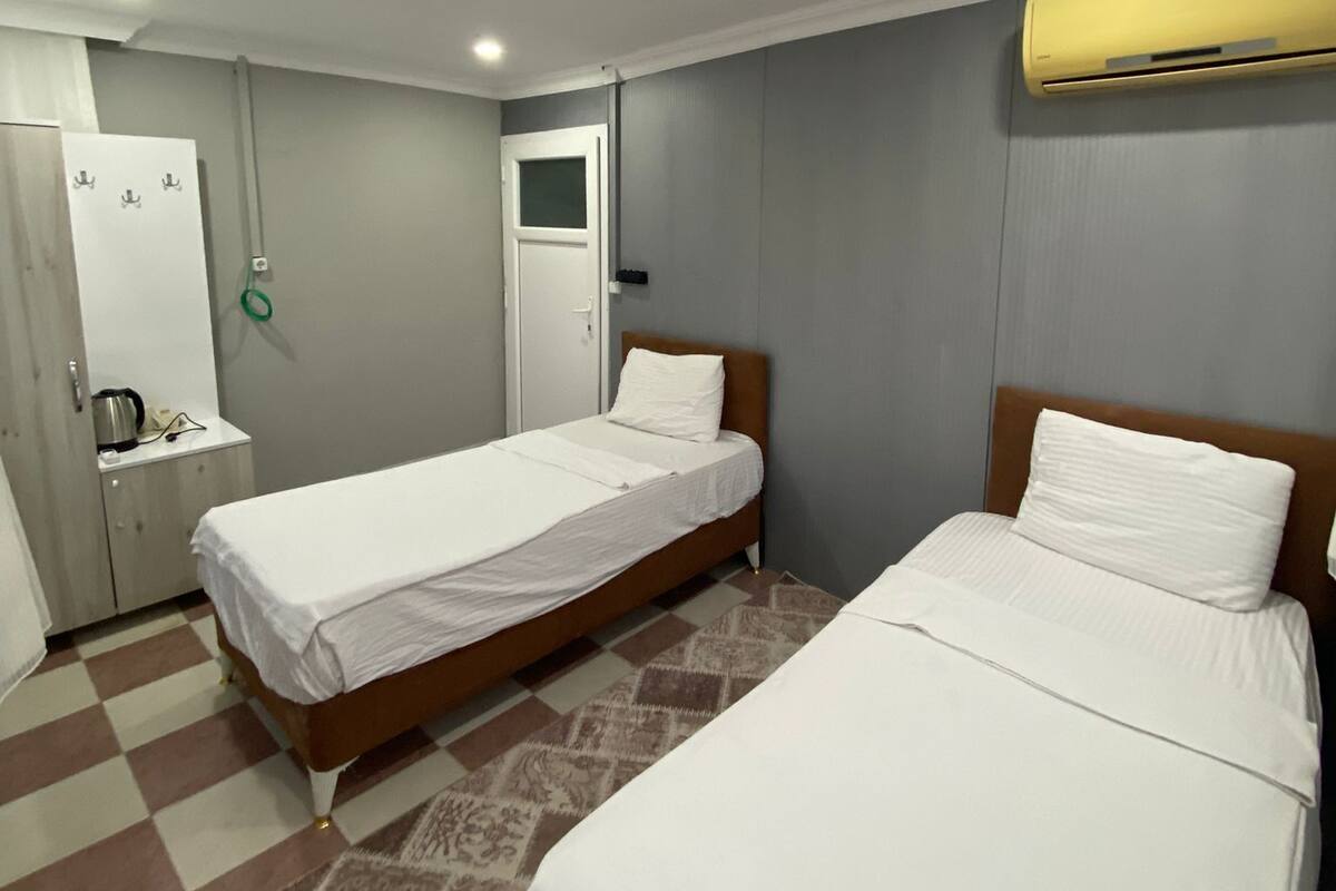 Ein Hotelzimmer mit zwei Einzelbetten, einem Kleiderschrank, einem Schreibtisch mit Wasserkocher und einer Klimaanlage.