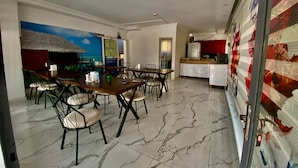 Un espace repas avec une grande table et des chaises, un coin cuisine équipé d’un réfrigérateur, et une fresque murale.