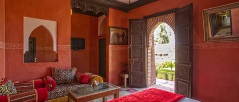 A room with a bed, a sofa, a table, and a door leading to a garden.