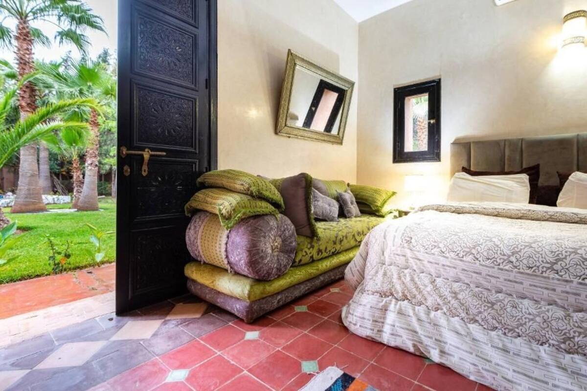 A bedroom with a large bed, a sofa with cushions, a door, and a wall-mounted mirror.