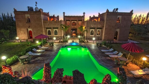 Vista de la piscina, un edificio, sillas de descanso y sombrillas.