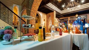 Disposición de un bufé con diversos alimentos y salsas sobre una mesa, frente a un fondo de paredes de ladrillo y arcos decorativos.
