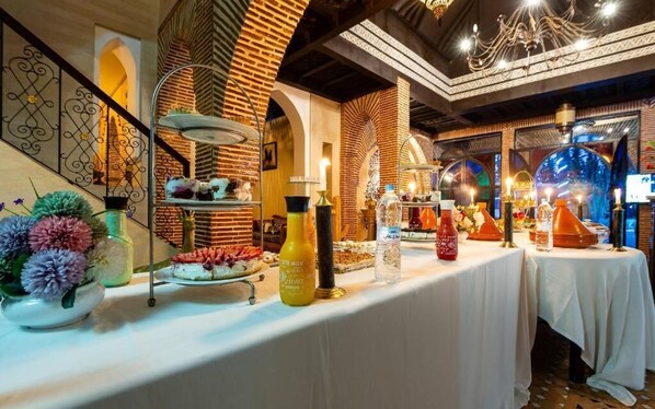 Disposición de un bufé con diversos alimentos y salsas sobre una mesa, frente a un fondo de paredes de ladrillo y arcos decorativos.