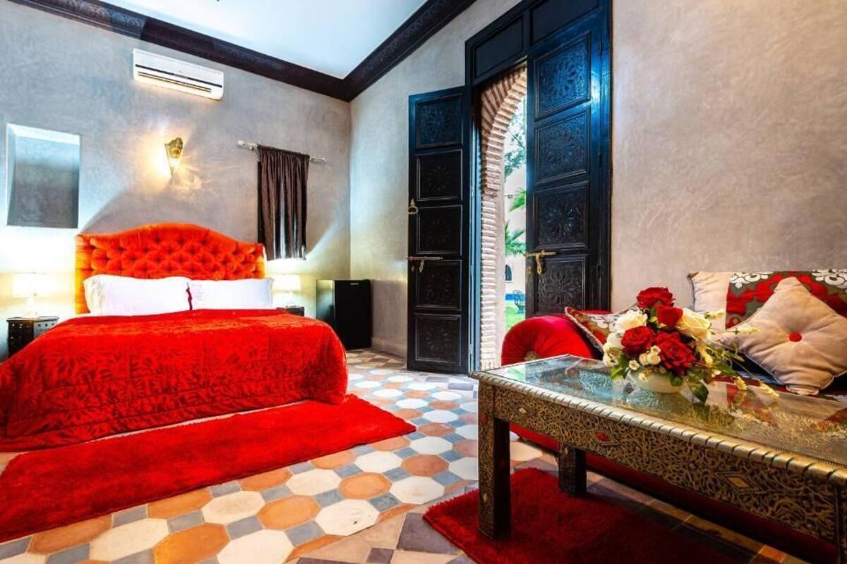 A hotel room with a large bed, a glass coffee table, and a view of the outside through a door.