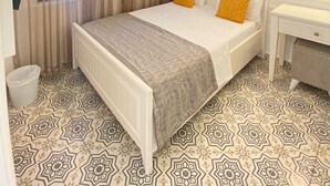 A hotel room with a bed, a desk, a television, and patterned flooring. - Bozcaada Butik Pansiyon (Bozcaada)