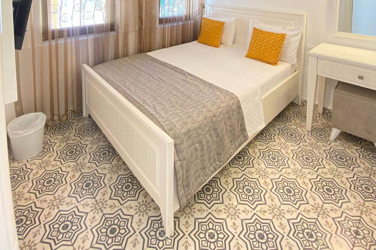 A hotel room with a bed, a desk, a television, and patterned flooring.