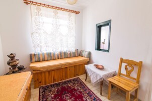 Una habitación acogedora con un banco de madera, una mesita con un cuenco, una silla, un tapete estampado y una lámpara decorativa.