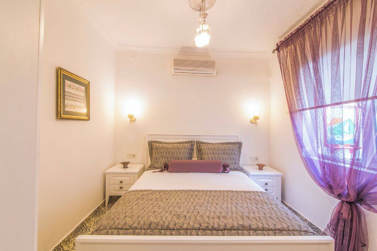 A neatly arranged bedroom with a bed, bedside tables, and a window with sheer curtains.