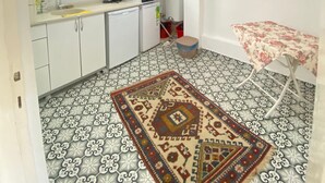 A compact kitchen with white cabinets, a microwave, and a sink. There's a patterned rug on the floor and a small table with a floral tablecloth. - Bozcaada Butik Pansiyon (Bozcaada)