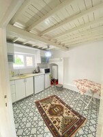 Cocina compacta con armarios blancos, microondas y lavabo. Hay una alfombra estampada en el suelo y una mesita con mantel floral.