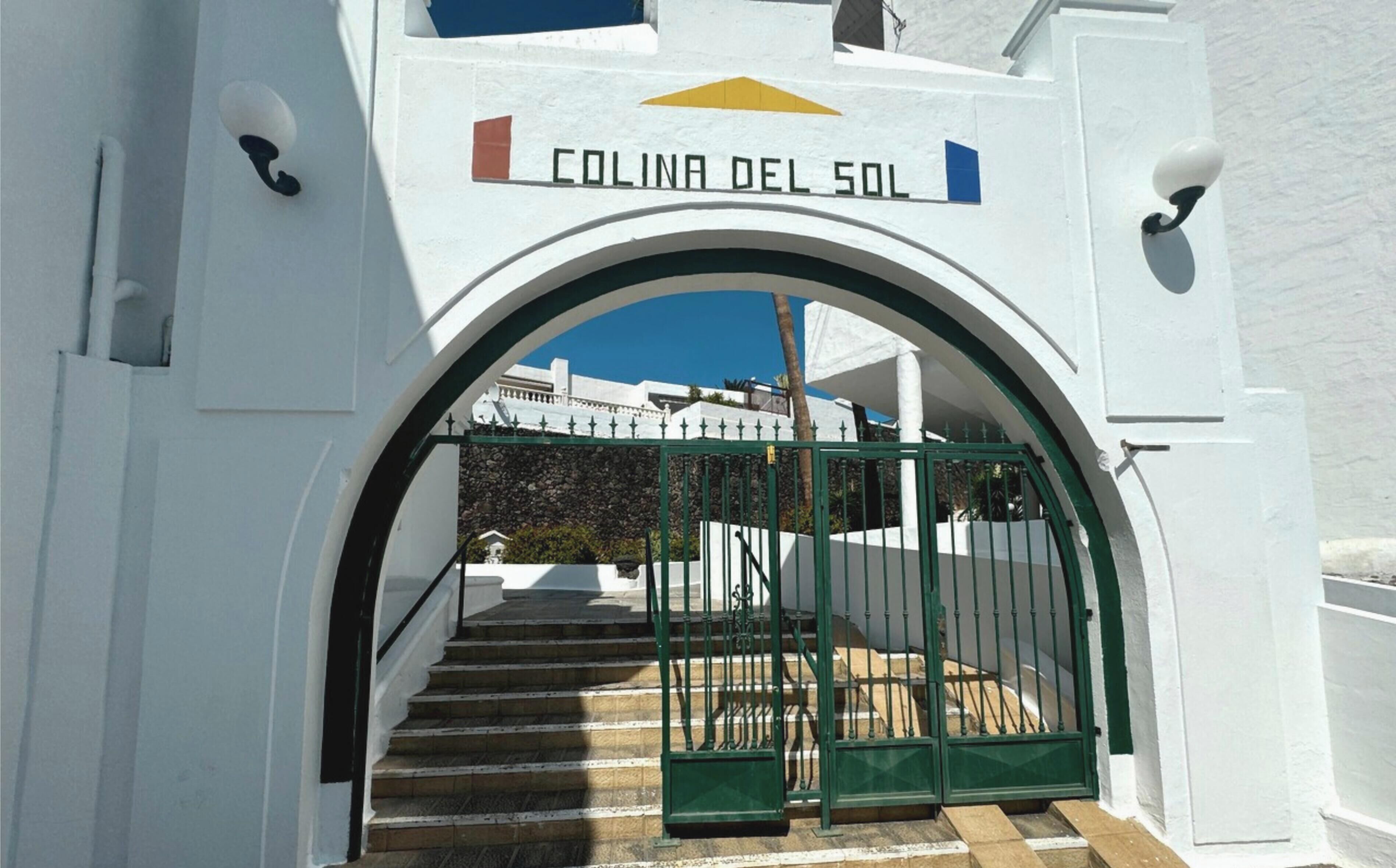 En vit byggnad med en skylt som visar texten ”COLINA DEL SOL” ovanför en grön port.