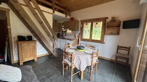 Une cuisine chaleureuse avec un coin repas, un escalier en bois et un téléviseur fixé au mur.