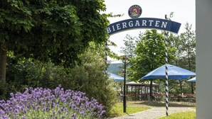 A sign for 'Biergarten' with a blue and white color scheme, surrounded by lush greenery and a gazebo structure in the background. - Hotel Imhof (Gemuenden)