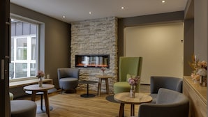 A modern lounge area with a stone wall, a fireplace, and comfortable seating. - Hotel Imhof (Gemuenden)