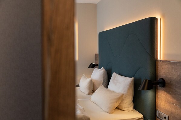 Habitación de hotel con una cama grande, cabecera oscura y dos lámparas de noche.