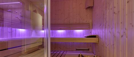A sauna with wooden walls and benches, a wooden bucket, and purple lighting.
