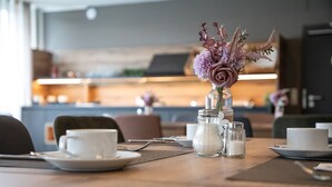 A dining table with white cups, a vase with flowers, salt and pepper shakers, and a candle holder. - Hotel Imhof (Gemuenden)
