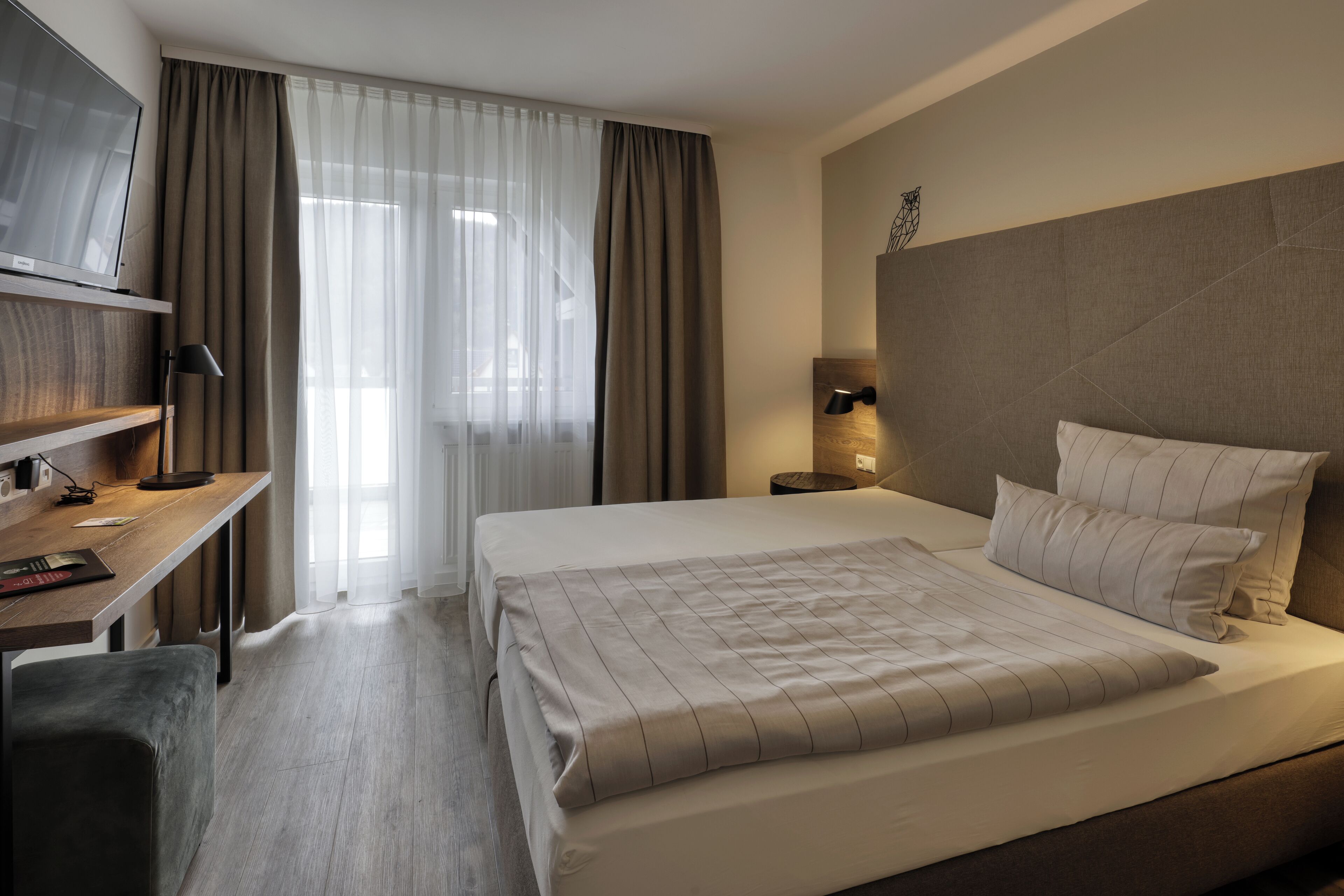 Habitación de hotel con una cama grande, un escritorio con silla, televisión y ventana con cortinas.