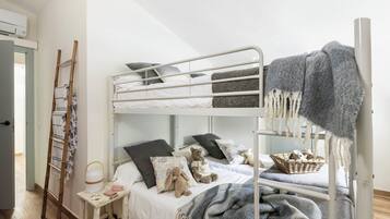 Una cama litera con escalera, una mesita de noche con lámpara, y una cesta en la litera inferior.