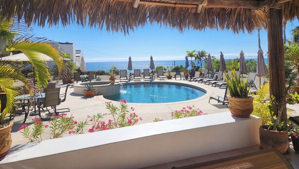 Un área de piscina con sillones de descanso y sombrillas, techo de paja y vista al océano.