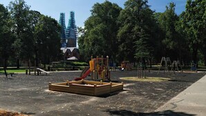 Un patio de juegos al aire libre con diversas estructuras recreativas, rodeado de árboles y un edificio en construcción al fondo.