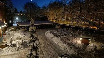 A snowy outdoor area with a covered seating area, a snow-covered tree, and a parked car.