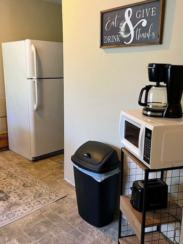 A kitchen with a white refrigerator, a black trash bin, a coffee maker, and a microwave. - 1 bed cottage, grill, fire pit, Very close to Red River Gorge!! (Stanton)