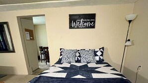 Een slaapkamer met een bed, een welkomstbord, een lamp en een deur.