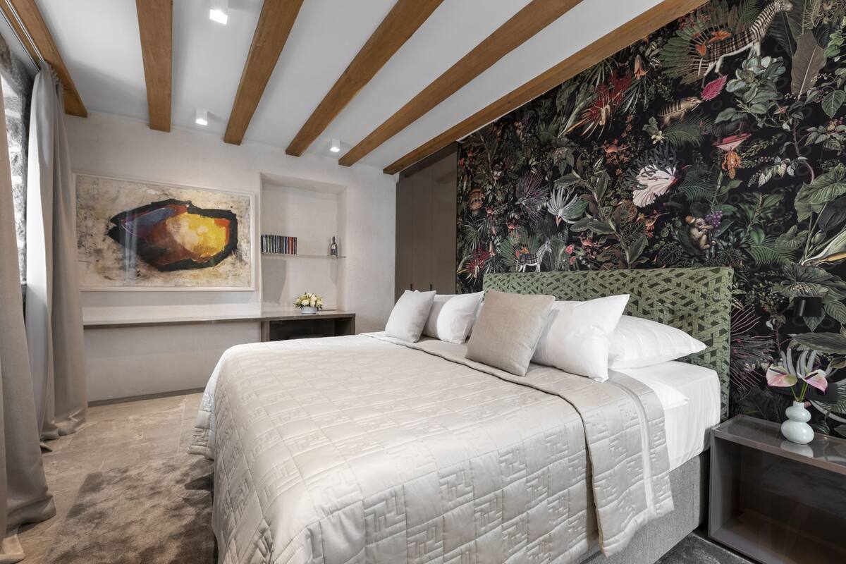 A bedroom with a large bed, a headboard with a floral pattern, and a wall with a tropical mural.
