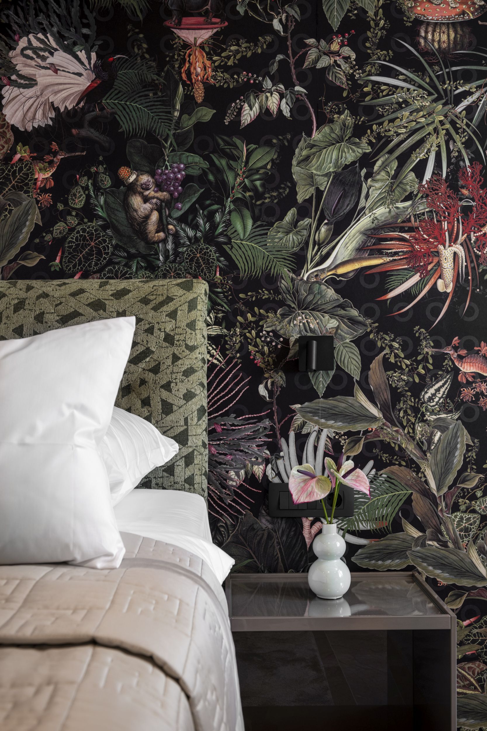 Ein Schlafzimmer mit einem Bett, Kissen, einem Nachttisch und einer Vase mit Blumen.