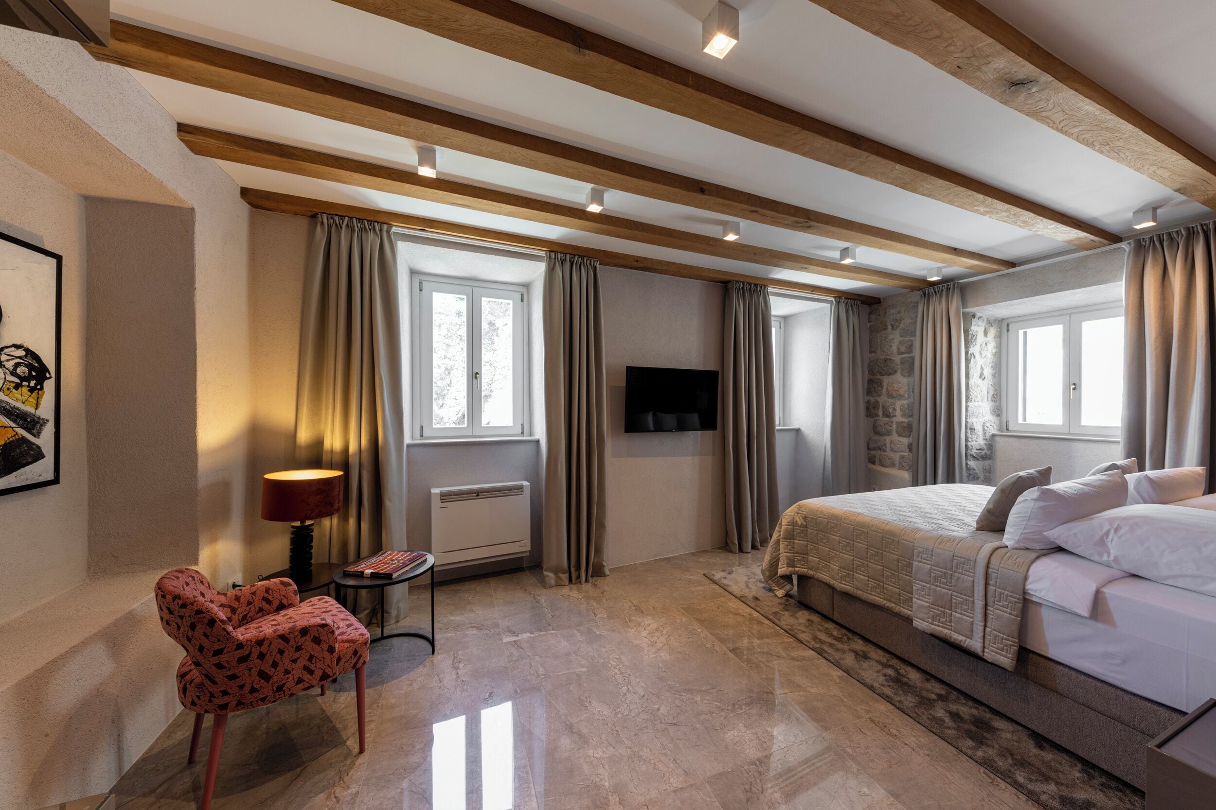 A hotel room with a bed, a chair, a TV, and a window with curtains.