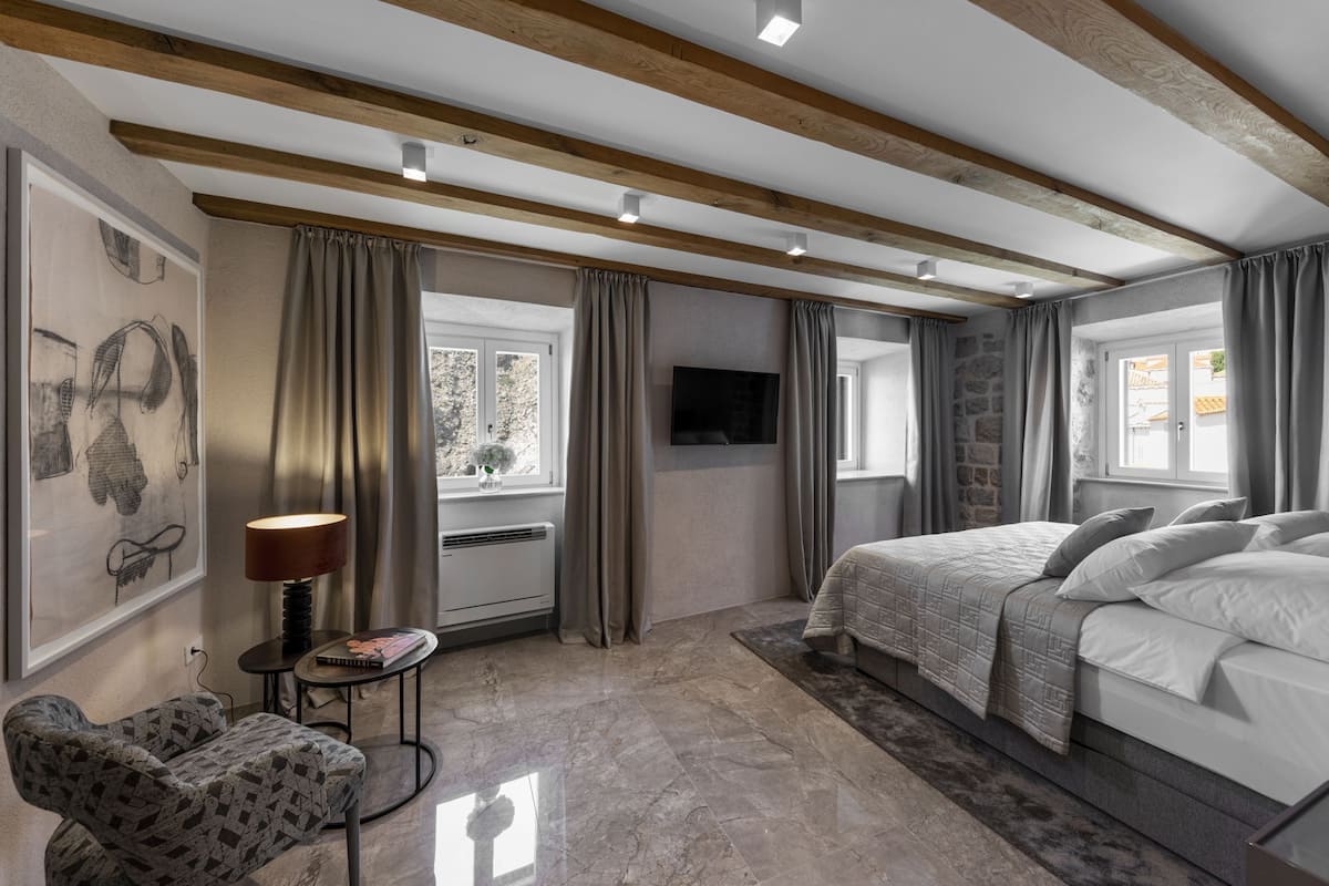A bedroom with a bed, a chair, a TV, and a window.