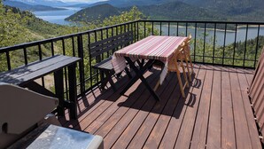 En træterrasse med et bord og stole, med udsigt over en sø og bjerge.