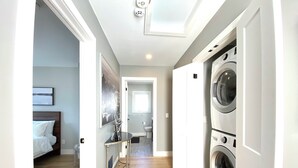 A hallway with a bed, a table, and a washing machine. - Near Ridley College  (St. Catharines)