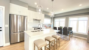 A modern kitchen with stainless steel appliances, a central island with stools, and a dining area with chairs. - Near Ridley College  (St. Catharines)