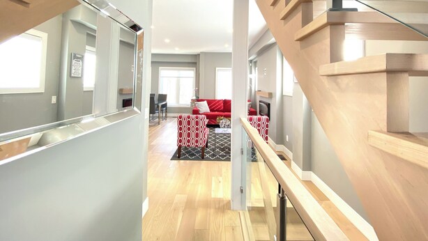 A modern interior with a wooden staircase, a red sofa, and a patterned ottoman. - Near Ridley College  (St. Catharines)