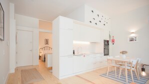 A modern kitchen with white cabinets, a dining area with a table and chairs, and a small rug on the floor. - Liiiving in Porto - Haven Pool Apartment (Porto)