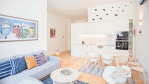 A modern living room with a sofa, a coffee table, and a dining area with chairs and a table. - Liiiving in Porto - Haven Pool Apartment (Porto)